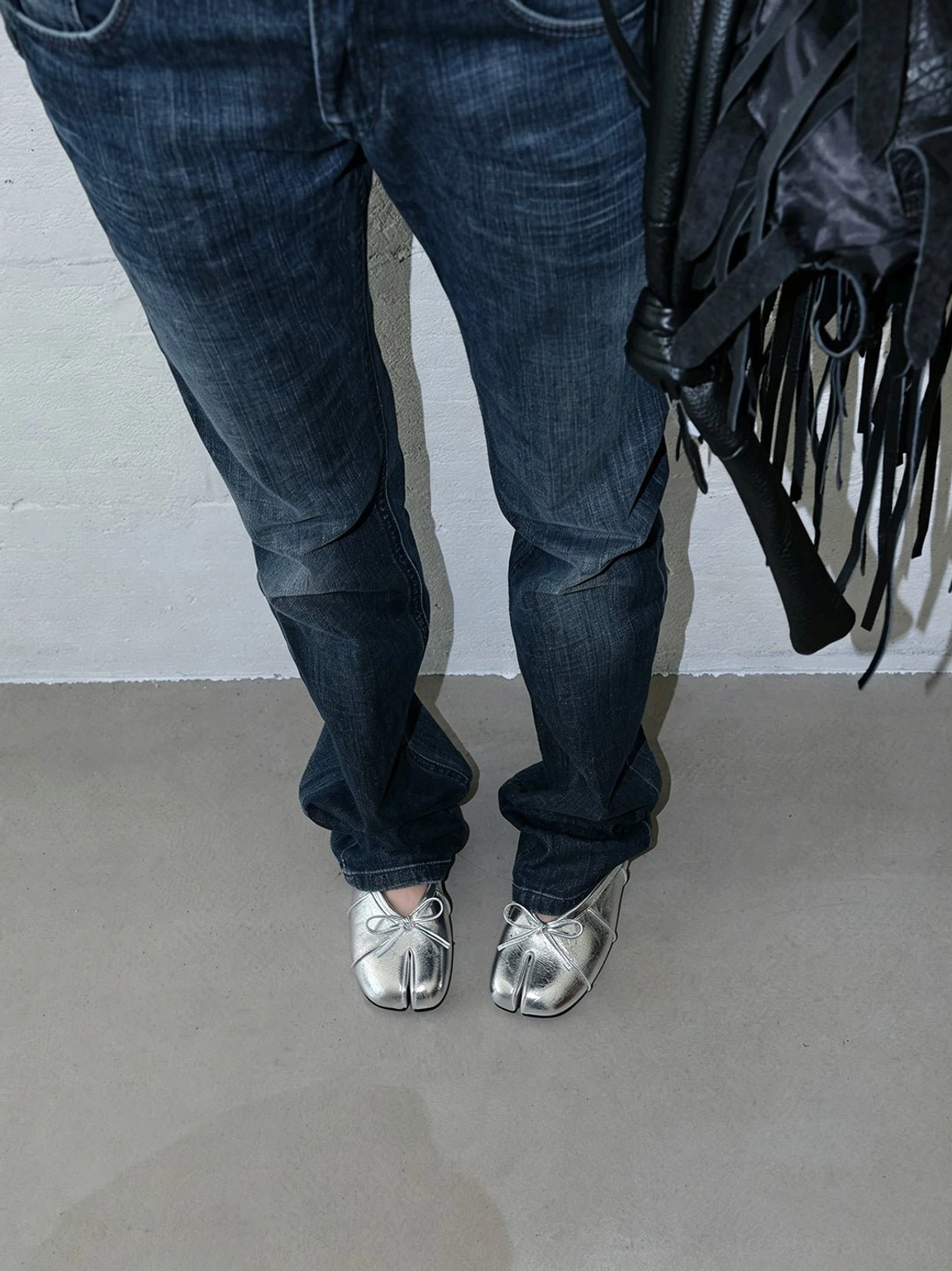 Full outfit view of metallic silver tabi toe bow mules styled with baggy jeans and a fringe backpack