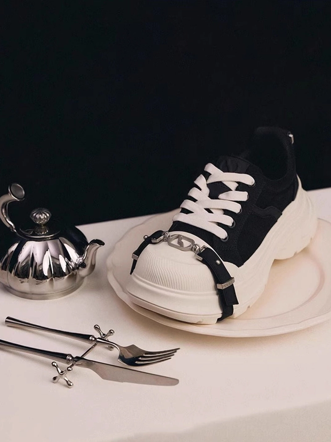 Front view of a single black canvas platform sneaker with silver D-ring buckle strap, white chunky sole, and contrast toe cap