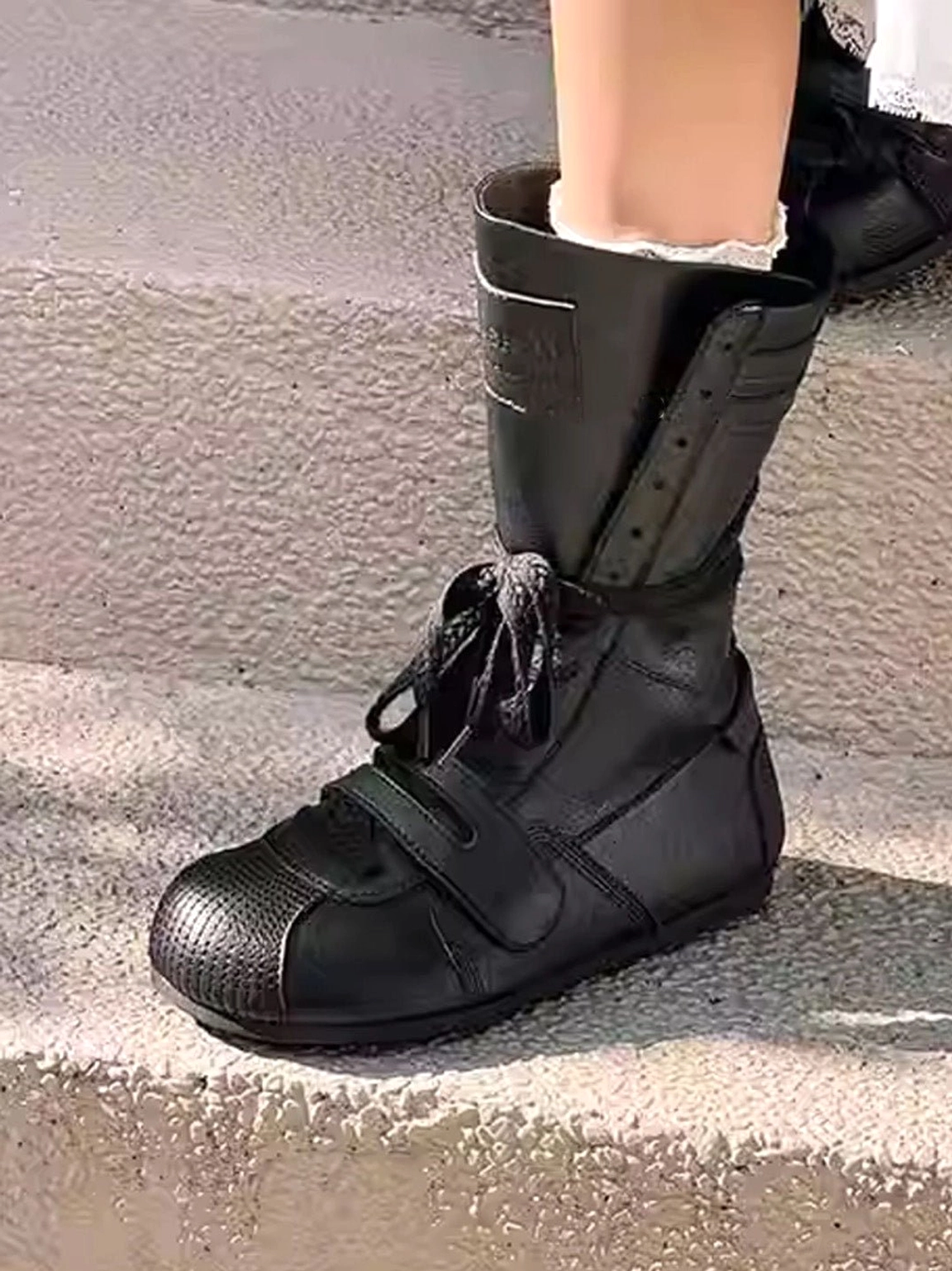 Single black leather-look boxing boot displayed on a concrete step with ribbed shaft, front strap, lace-up closure, and elevated platform sole