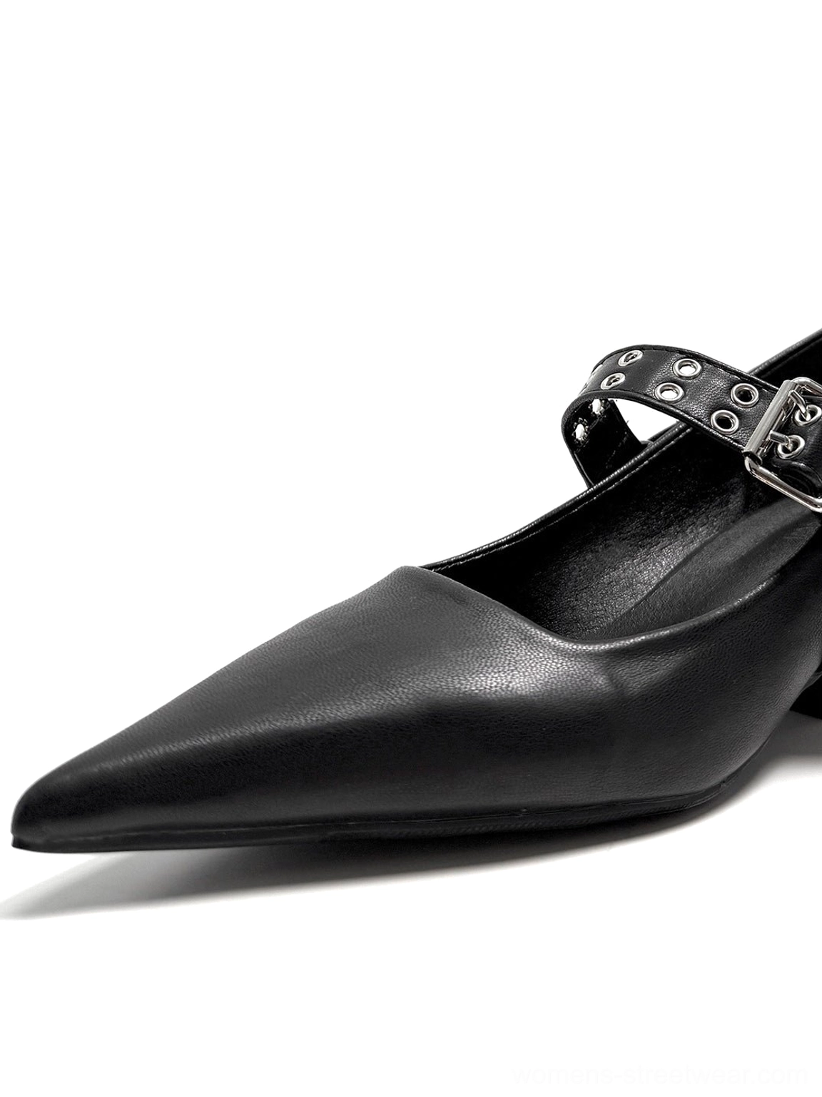 Close-up of a single black pointed Mary Jane pump showing the smooth upper, grommet strap, metal buckle, and sharp toe