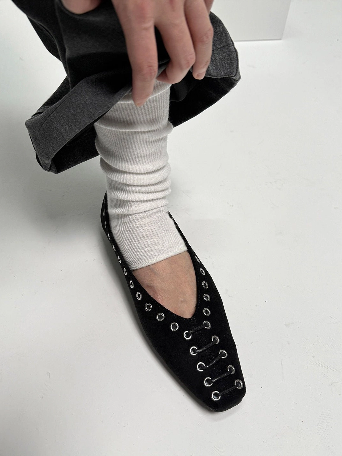 Single black square-toe ballet flat worn with a white slouch sock and grey oversized trousers
