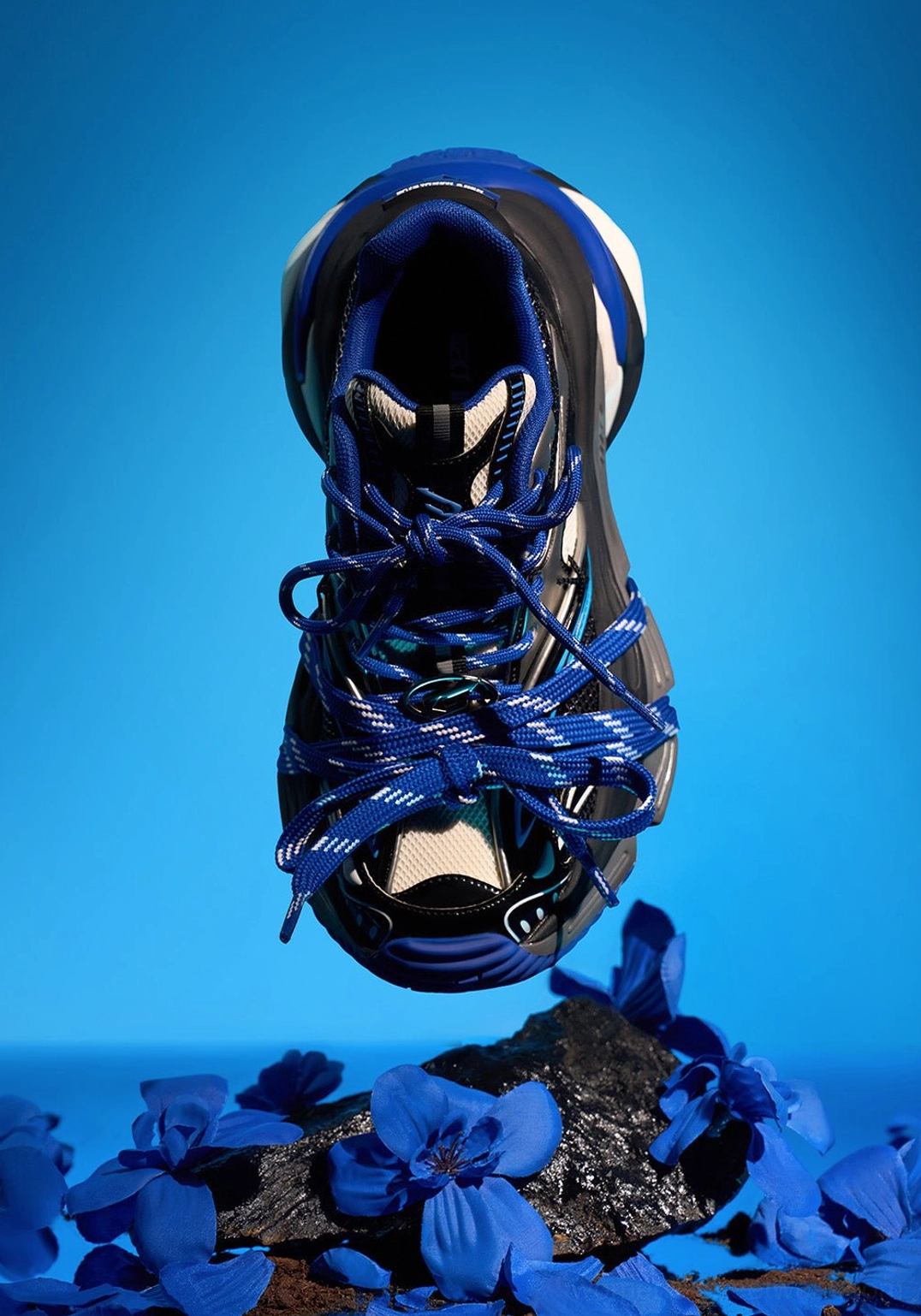 Single blue chunky platform sneaker displayed from a top-down angle with wrapped blue laces, silver reflective panels, and translucent-looking sole accents