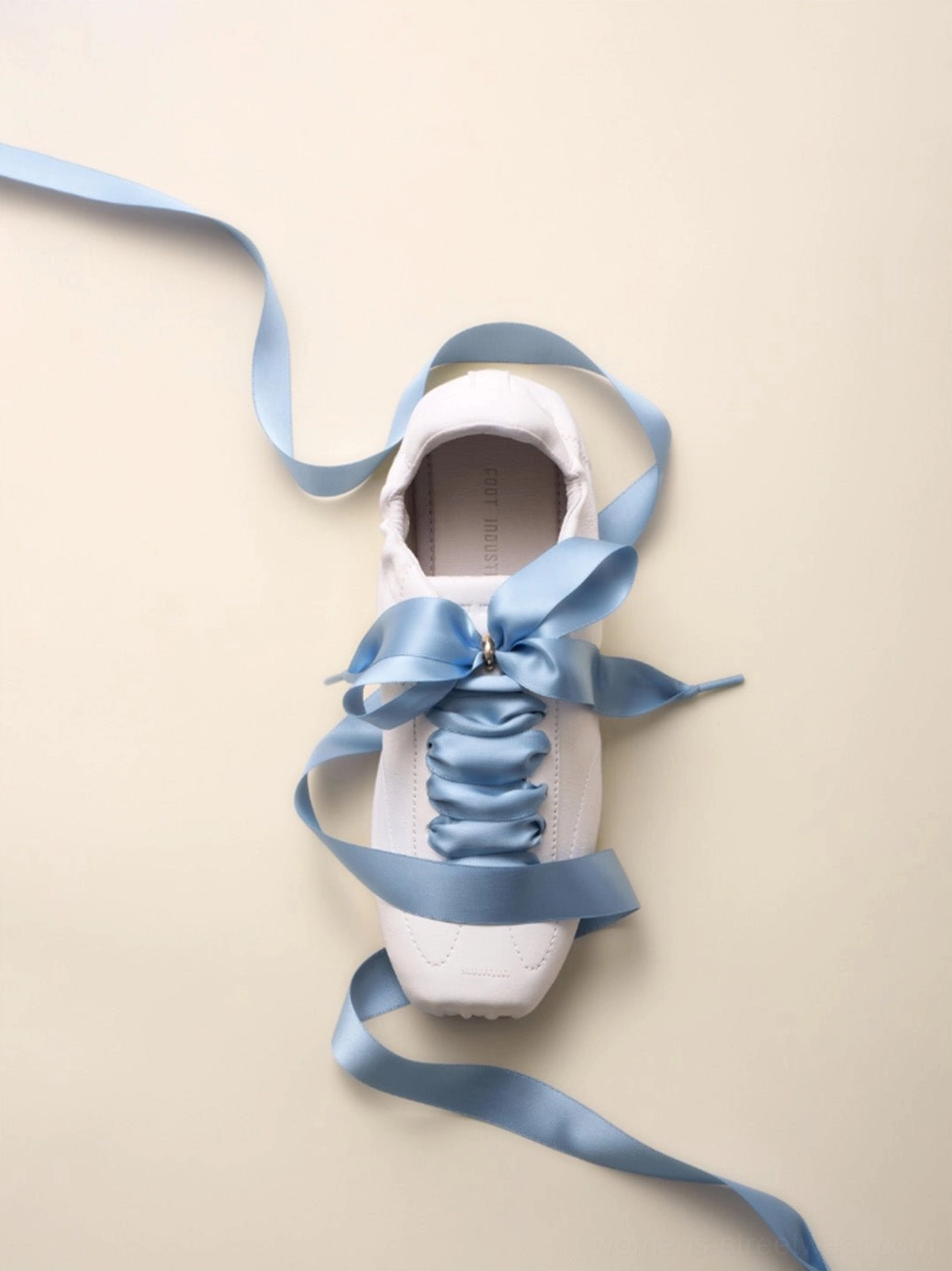 Single white low-profile retro trainer with flowing sky blue satin ribbon laces in a modern streetwear product close-up
