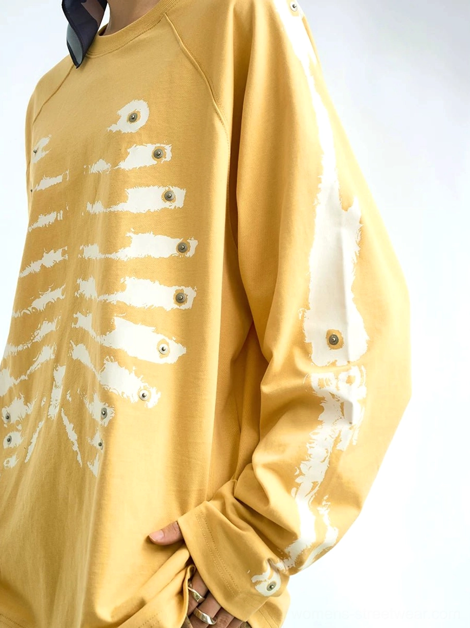Close-up of yellow skeleton graphic raglan streetwear shirt showing bone print, metal eyelet details, and exposed raglan seams