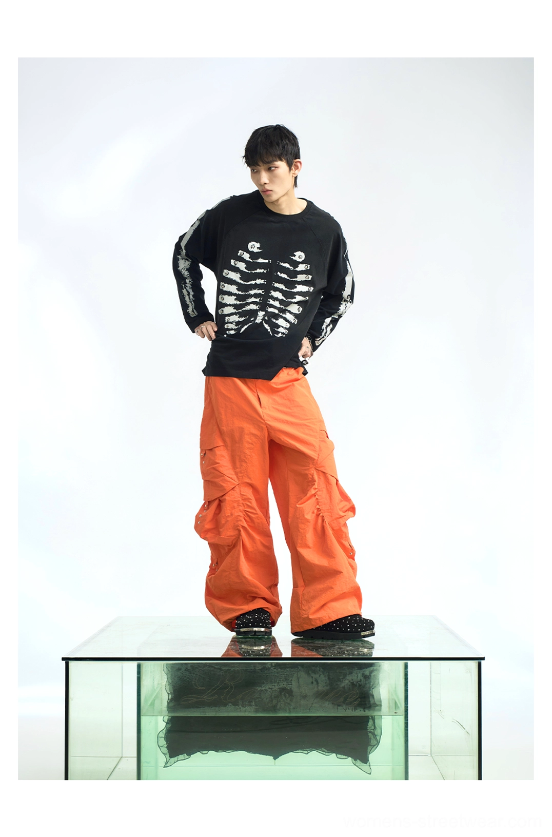 Black skeleton chest print raglan long sleeve streetwear t-shirt paired with bright orange wide-leg cargo pants in a full-body look