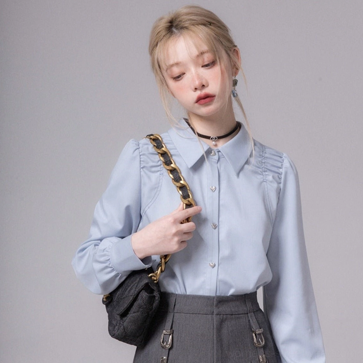 Three-quarter view of sky blue heart button blouse with ruched shoulders pointed collar and chain bag