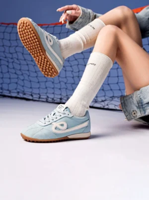 Woman wearing sky blue quilted gum sole retro streetwear sneakers with white crew socks on badminton court