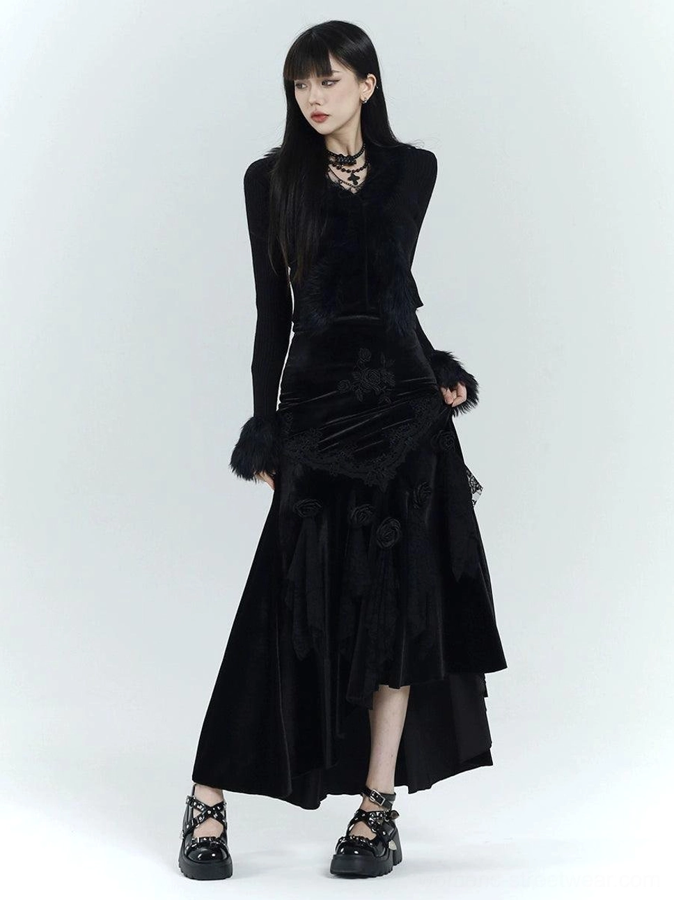 Three-quarter view of a slim-fit gothic velvet fishtail dress with asymmetric hem, embroidered flowers, lace accents, and faux fur cuffs