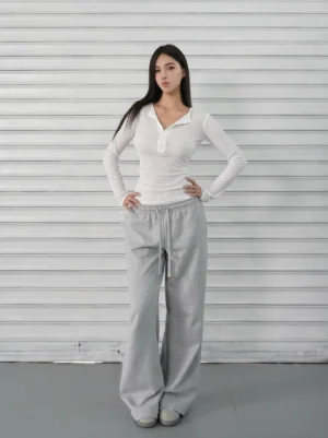 White slim-fit ribbed Henley long sleeve top shown in a full-body front view with grey wide-leg sweatpants and casual flat shoes