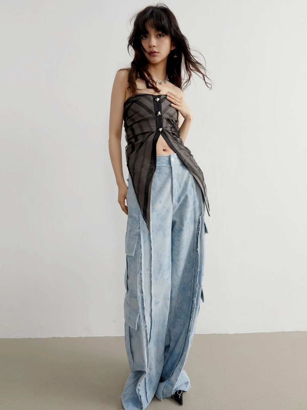 Full front view of a slim-fit strapless studded tube top with exposed waistline and acid-washed utility jeans