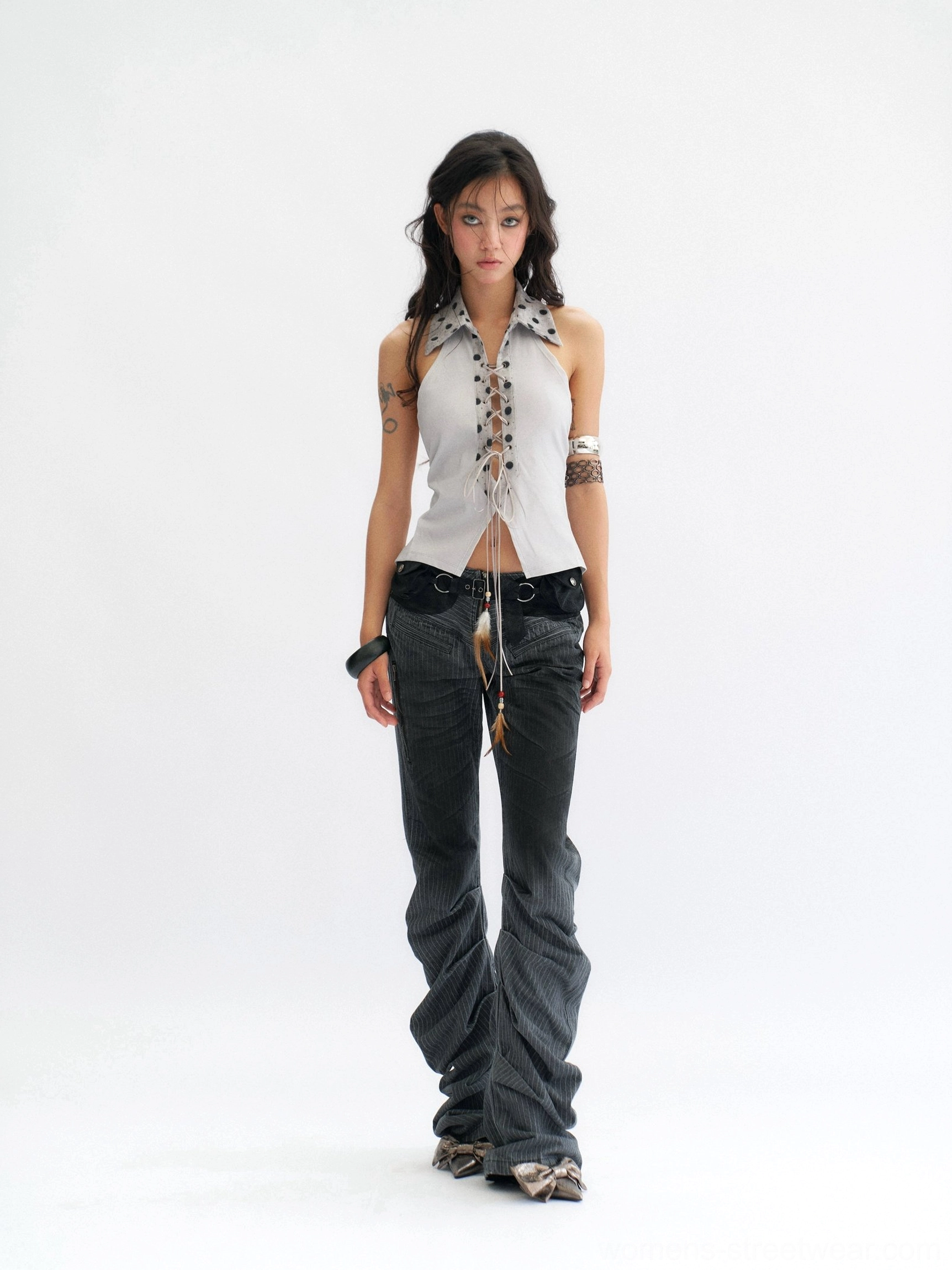 Front view of a smoke blue-gray polka dot lace-up halter top with cropped corset silhouette and feather-inspired tassel detail styled with low-rise flared jeans