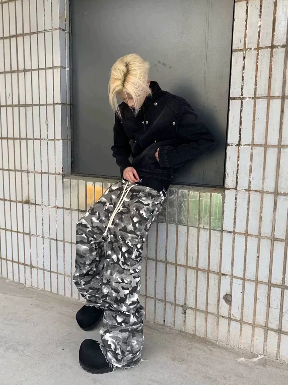 Side view of loose smoke grey camouflage wide leg streetwear pants with drawstring waist styled with a cropped black jacket
