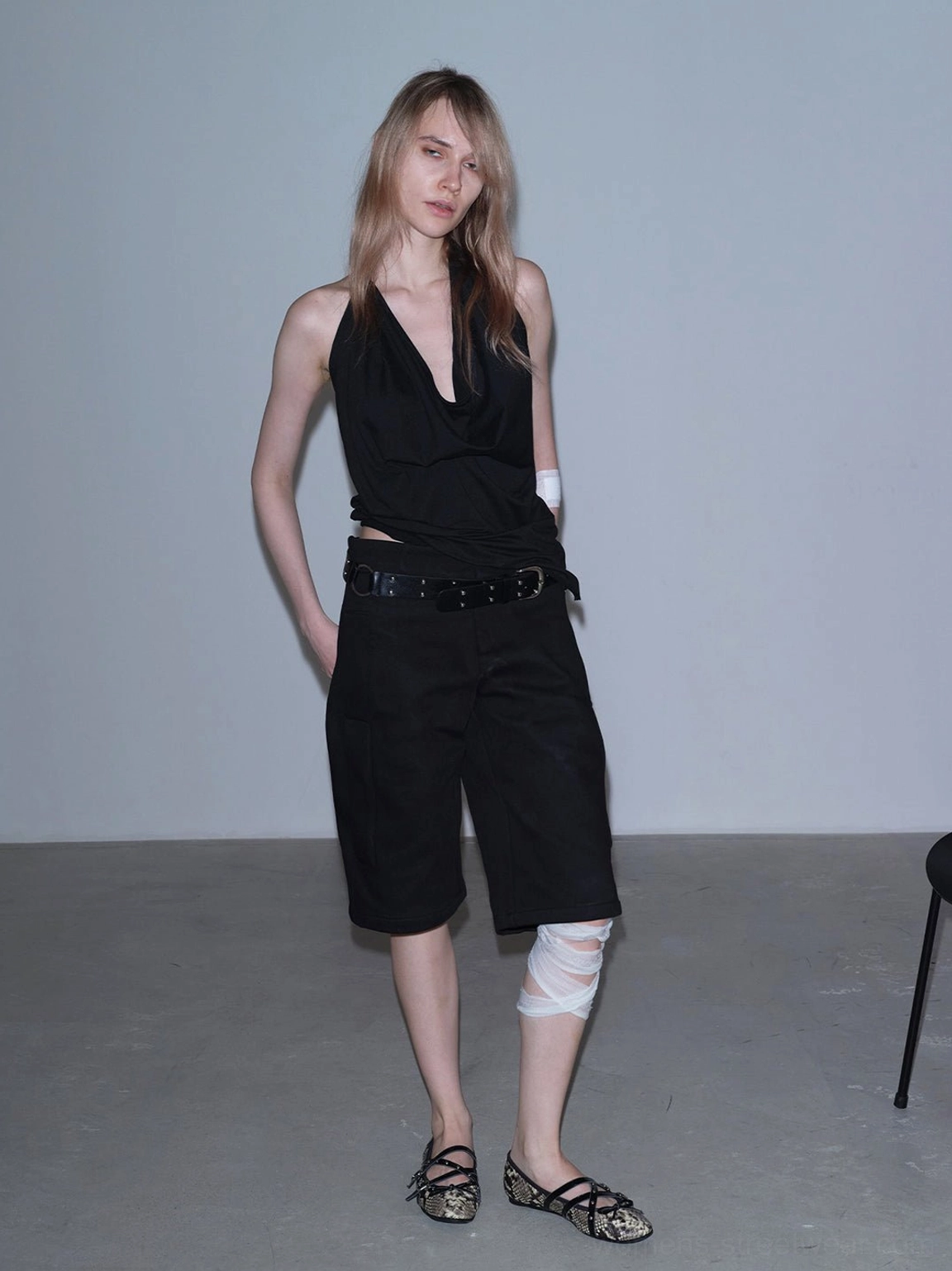 Snakeskin cross-strap ballet flats paired with black halter top and shorts in minimalist dark streetwear look