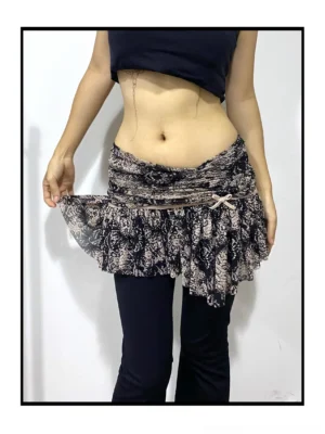 Three-quarter view of a women’s snakeskin drape mini skirt with folded ruched waistband, adjustable ribbon bow detail, irregular ruffle hem, and edgy streetwear styling