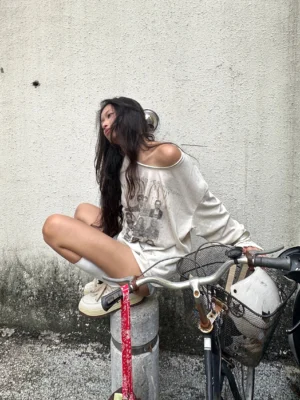 Side back view of apricot snowfall scimitar sleeve vintage graphic long sleeve tee styled with streetwear pants outdoors beside a bicycle