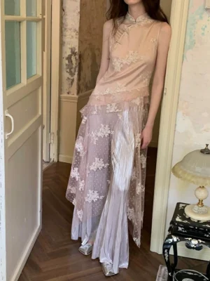 Full-body side view of a soft blush embroidered cheongsam-inspired wide-leg jumpsuit with floral mesh overlay and elegant silver pointed-toe heels