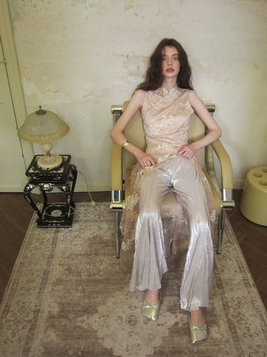 Front seated view of a soft blush floral embroidered Mandarin-collar jumpsuit with layered wide-leg trousers styled in a vintage interior
