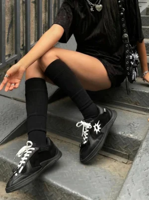 Black and white solar star applique court sneakers styled with an all-black outfit and knee-high socks in an urban stairwell