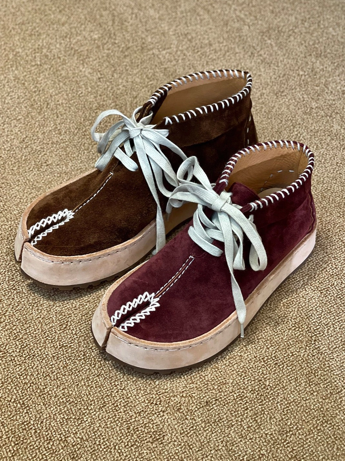 Dark brown and wine red split-toe leather chukka boots displayed on a textured brown carpet with contrast hand stitching