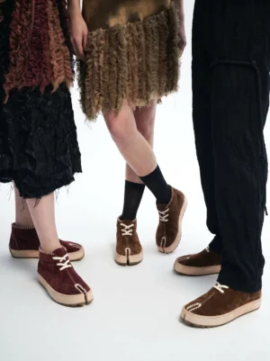 Unisex split-toe leather chukka boots in dark brown and wine red styled with textured streetwear outfits in a studio setting