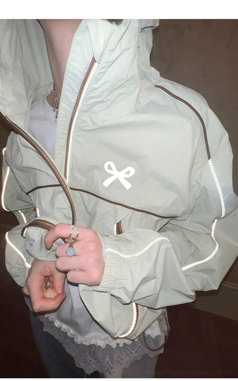 Close-up of lightweight sporty windbreaker jacket showing chest bow embroidery, half-zip closure, smooth fabric, and contrasting edge piping