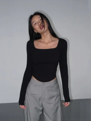 Black square neck ribbed crop top with long sleeves, slim fit, curved ruched hem, and Korean streetwear styling shown in a front full body view