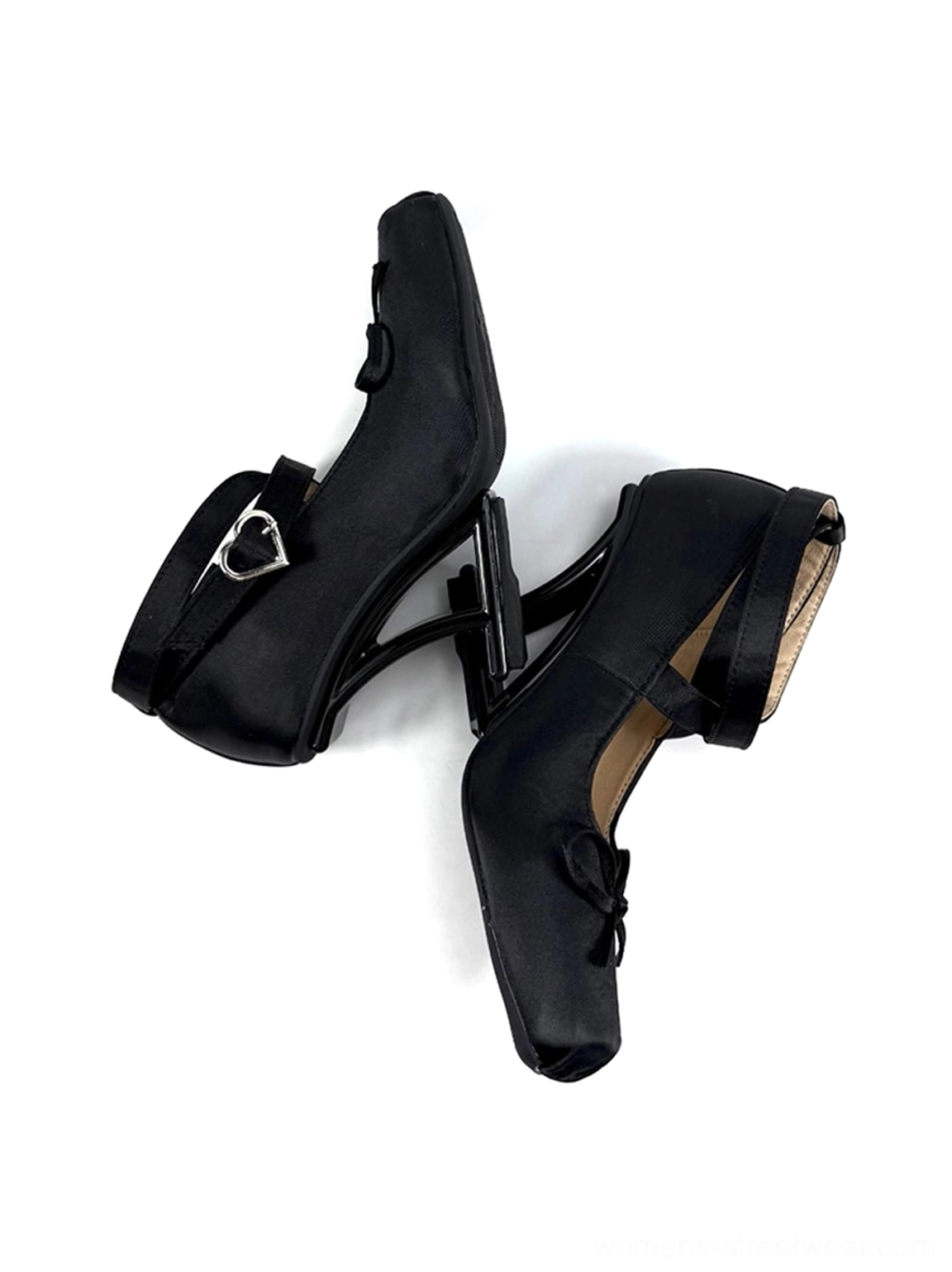 Stacked pair of black satin bow strap pumps showing the heart-shaped buckle, square toe, satin finish, and sculptural heel