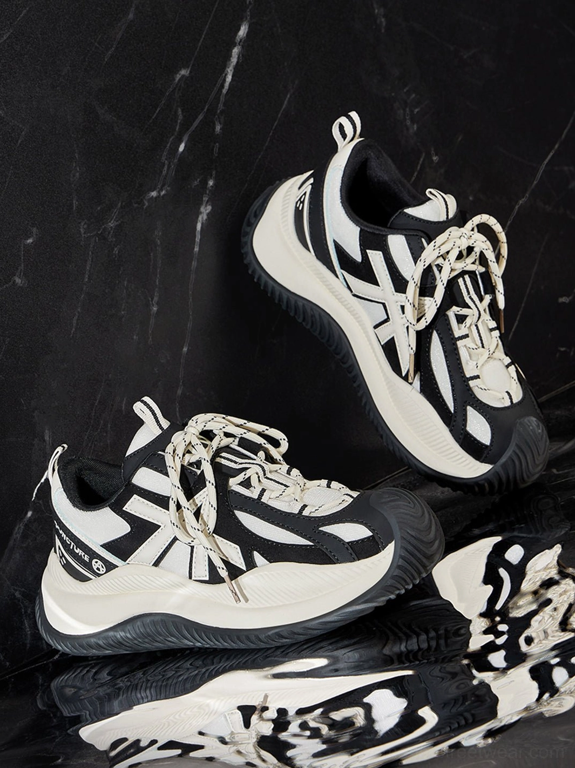 Oblique flat lay of chunky sneakers on black marble surface showing thick woven round laces and brand heel counter lettering