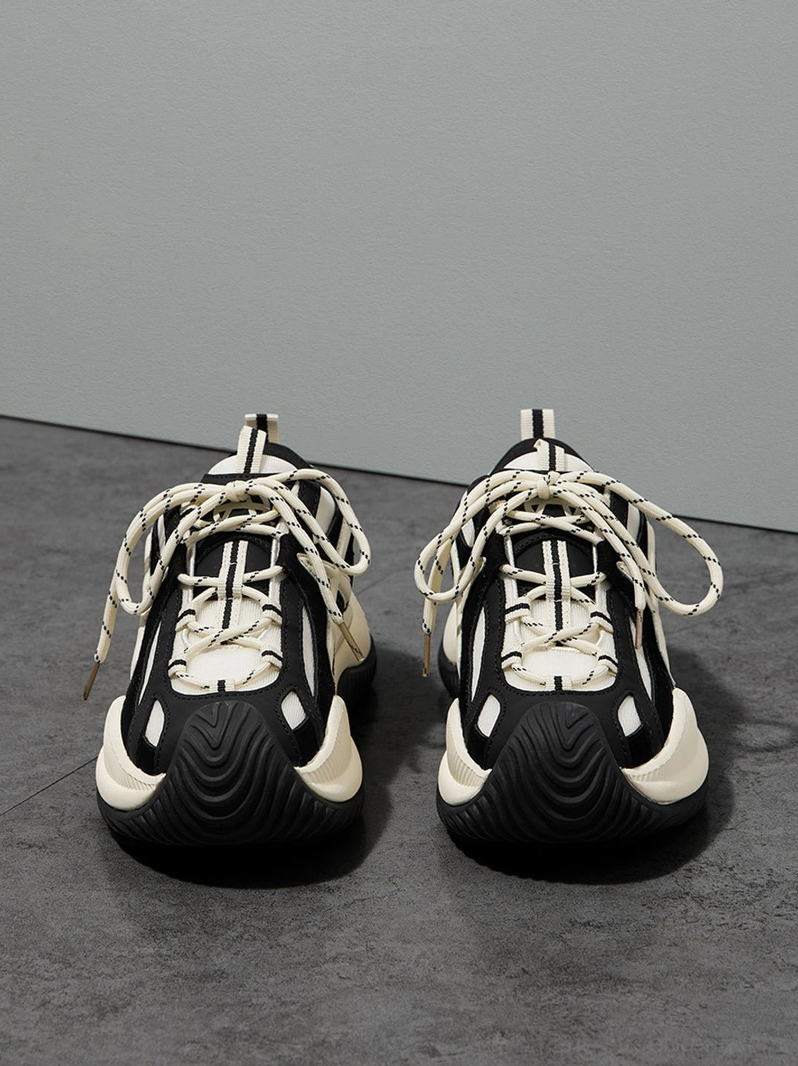 Frontal flat lay of chunky sneakers featuring symmetrical view black rubber toe cap white midsole and thick lace setup