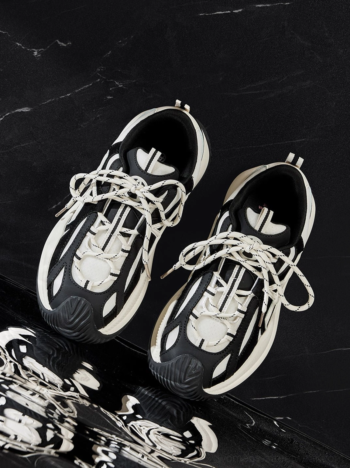 Top-down symmetrical dual sneaker display on marble background emphasizing cross upper motif and contrasting black white color palette