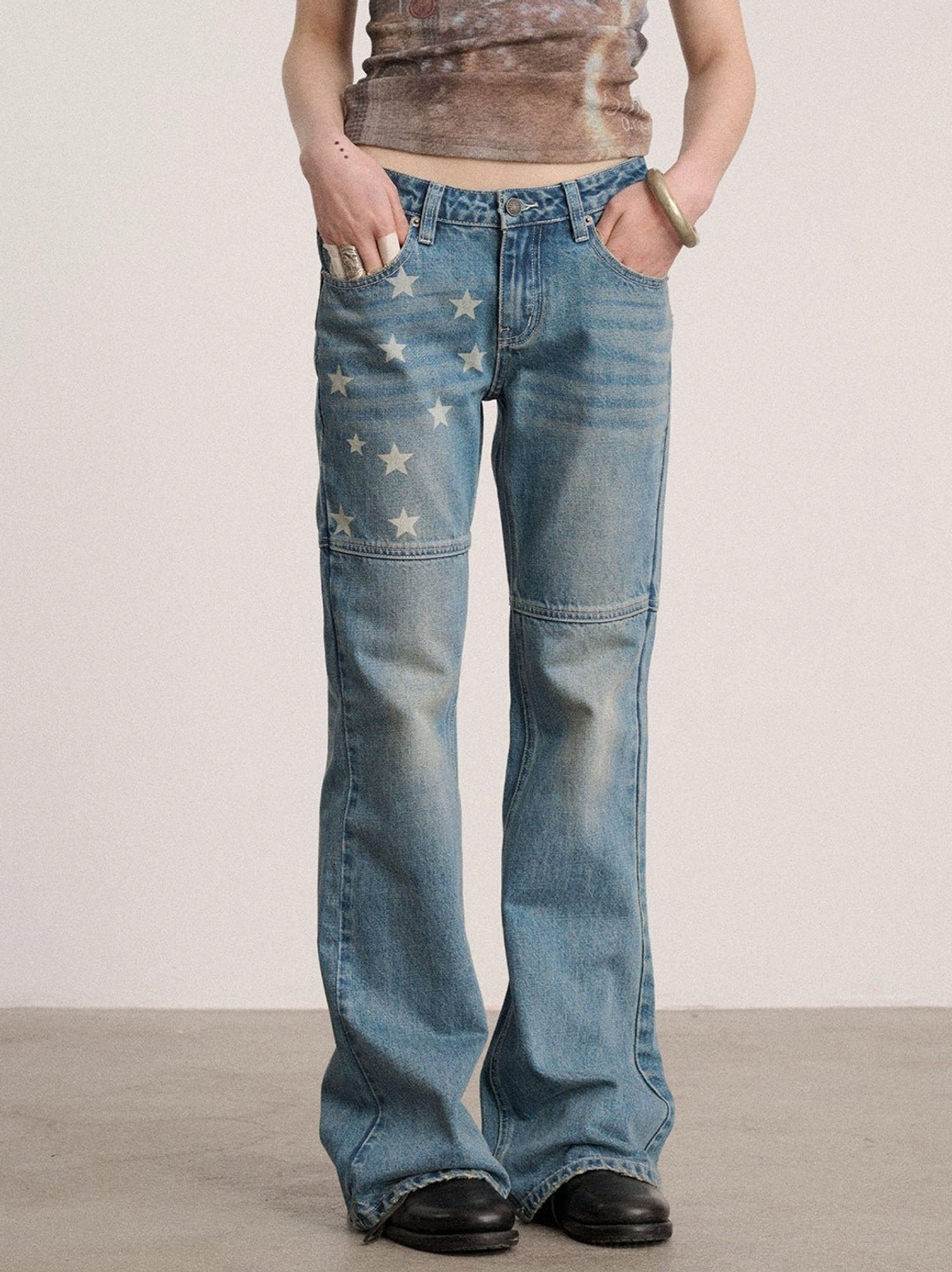 Front view of blue low-rise star panel flare jeans with faded denim wash, fitted upper leg, white star graphics, and flared hems