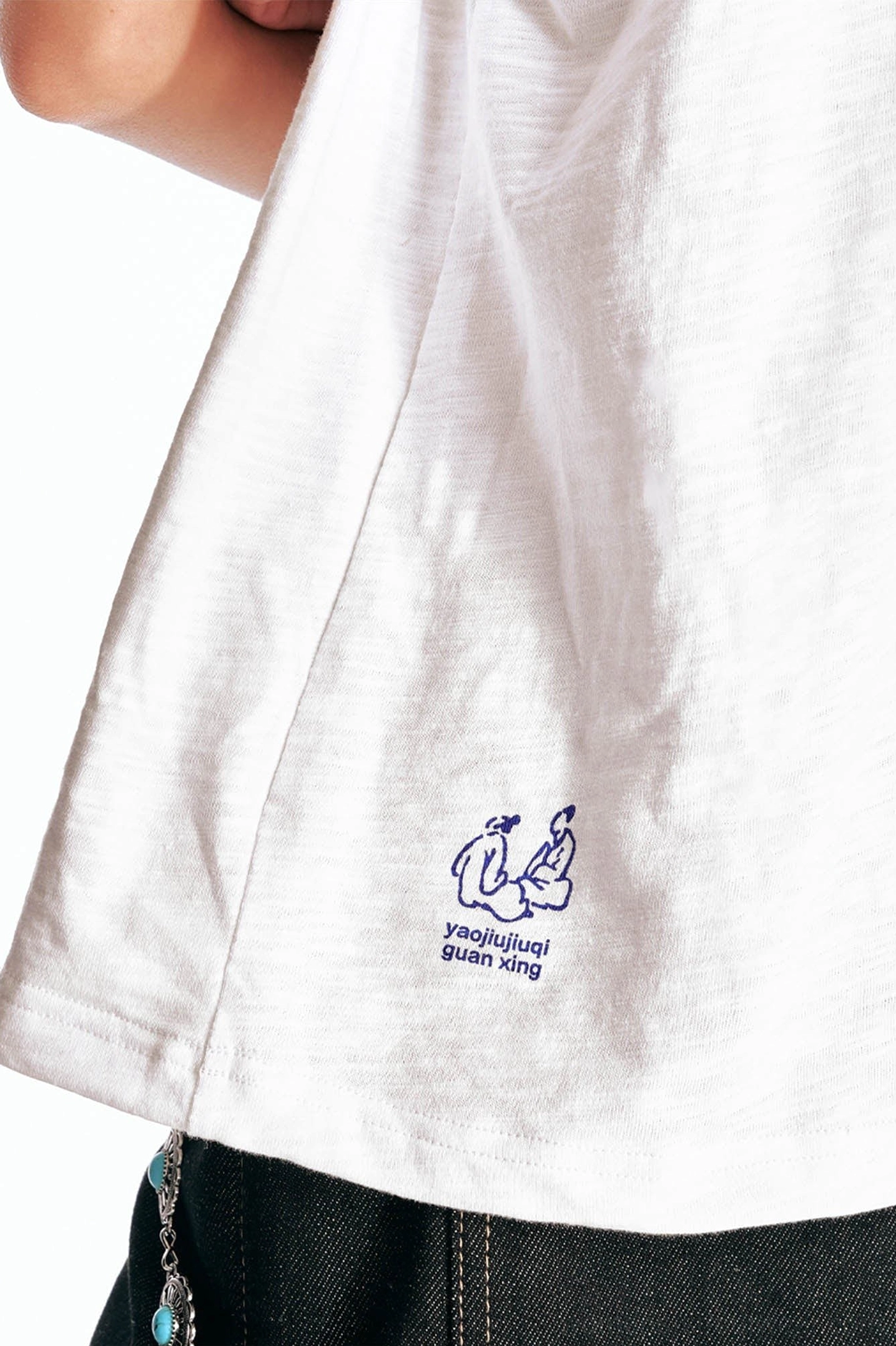 Close up of white star parade graphic cotton tee hem with small embroidered cartoon logo and textured cotton fabric