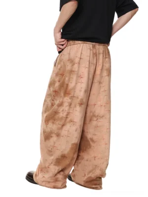 Rear side view of oversized star pattern satin streetwear trousers showing the wide leg silhouette, side pocket, rust starburst print, and relaxed unisex inspired fit