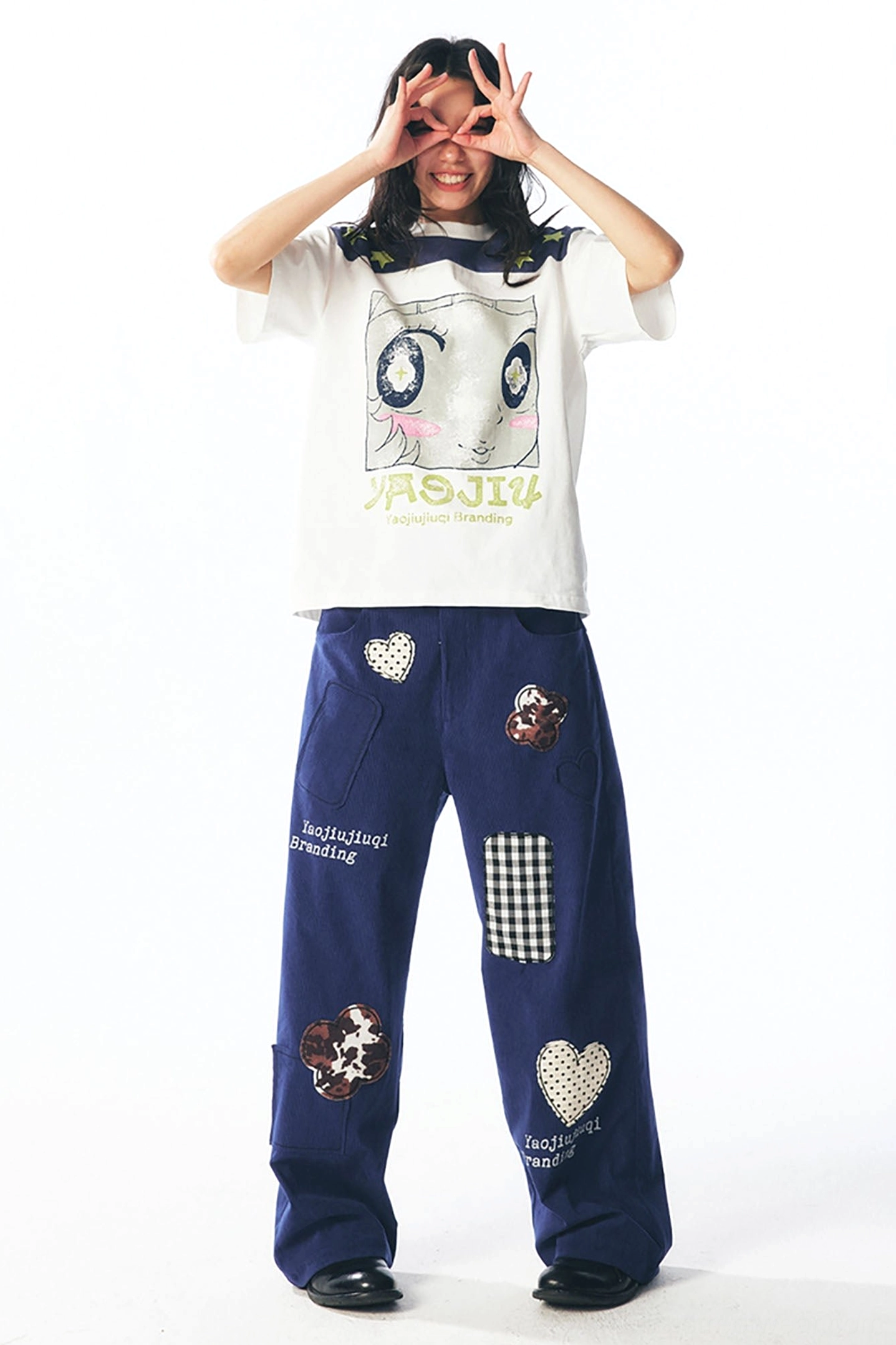 Female model styling white cartoon face graphic tee with navy star shoulder yoke and patchwork pants