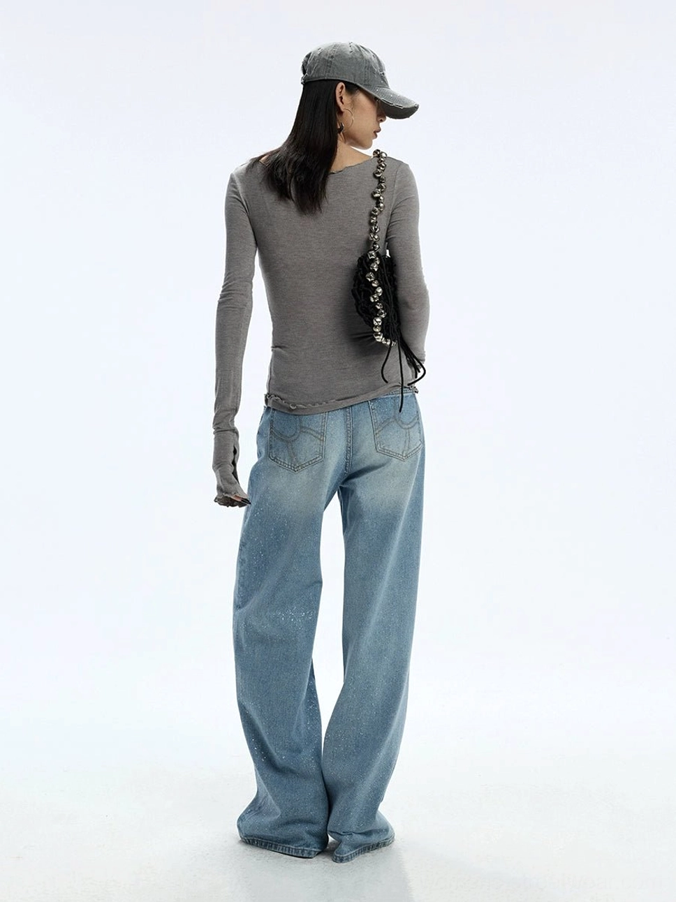 Back view of stardust glitter wide-leg jeans styled with a gray top, baseball cap, and chain shoulder bag