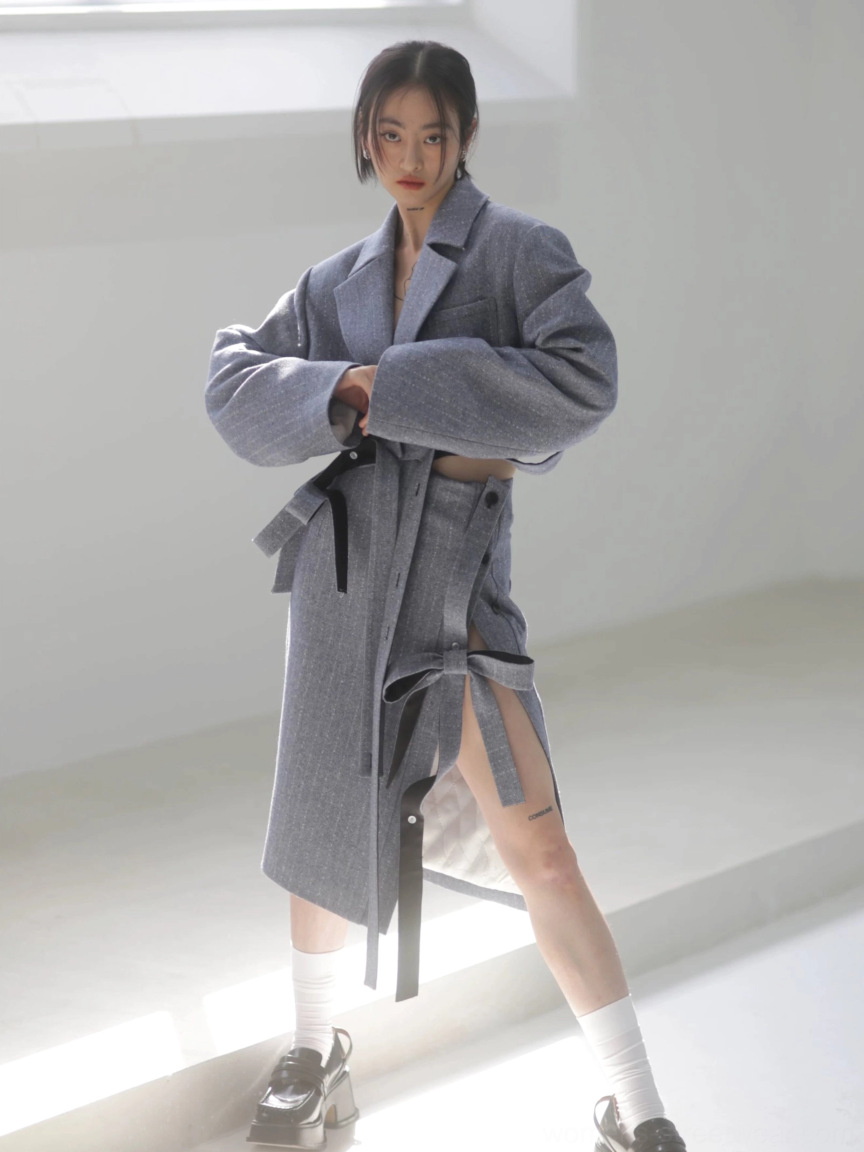 Front view of a steel blue grey herringbone pencil midi skirt and tailored coat outfit, highlighting the refined waistline, side opening, and modern streetwear styling