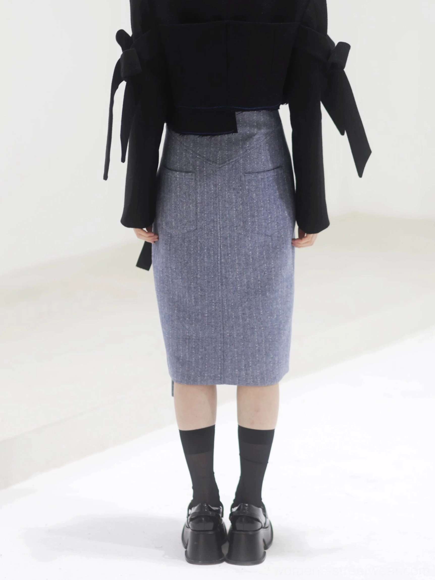 Back and lower-body view of a steel blue herringbone tailored midi skirt with a straight pencil shape, textured suiting fabric, and sleek structured finish