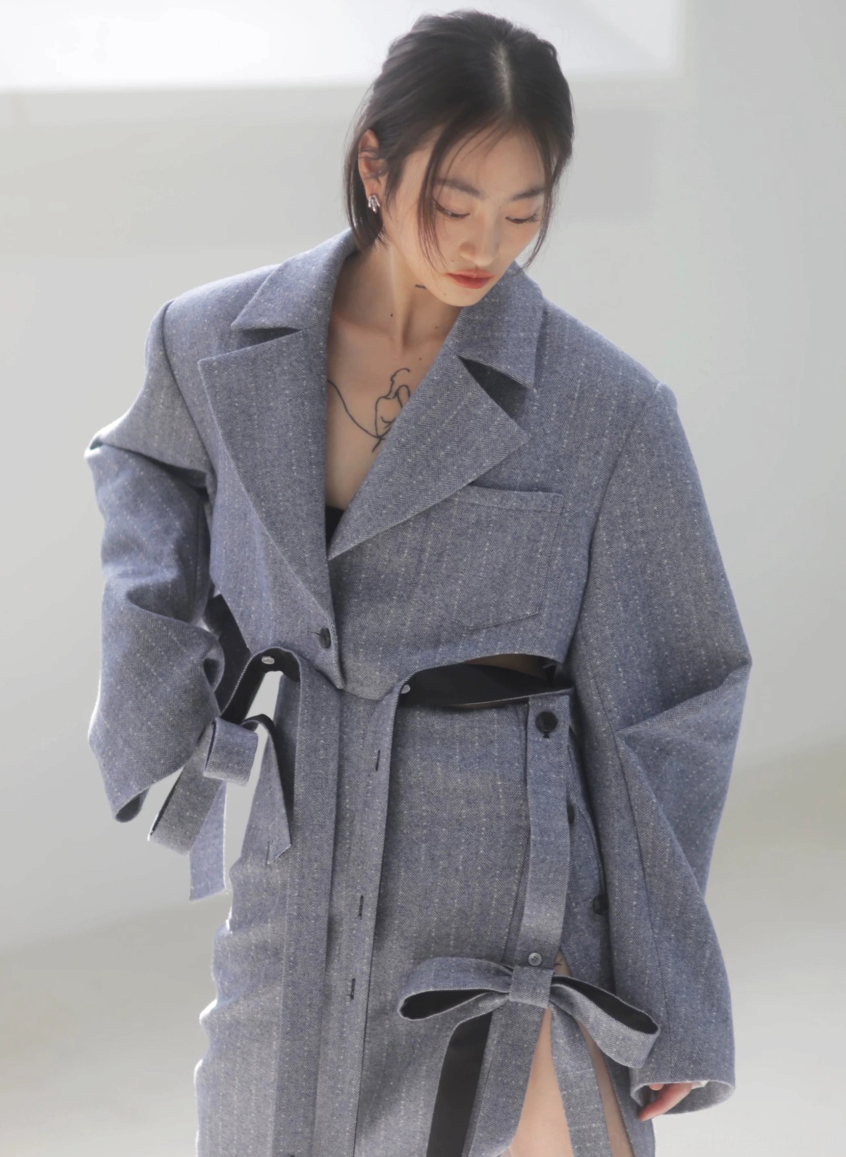 Close-up of steel blue herringbone tailoring with a notched lapel coat and matching pencil midi skirt, highlighting textured suiting and ribbon belt details