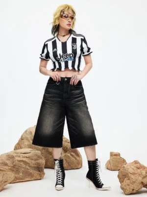 Female model full-body wearing black and white canvas stiletto boots with striped cropped football jersey and washed black denim culottes, studio setting with decorative rock props showcasing complete streetwear outfit