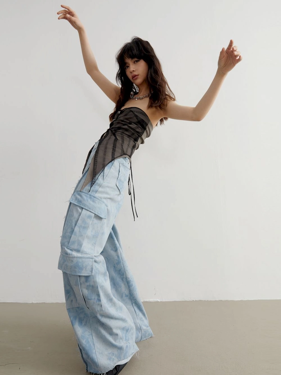 Dynamic side view of a strapless sheer asymmetric tube top with adjustable back tie detail and wide-leg cargo pants