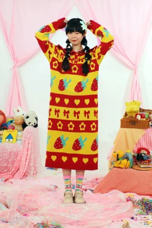Front full body view of a strawberry jacquard cotton knit sweater dress with sailor collar, red and yellow cartoon motifs, and relaxed long silhouette