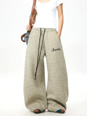 Female model wearing striped fleece wide-leg streetwear pants with a white tee, drawstring waist, side pockets, and crossbody bag in a studio