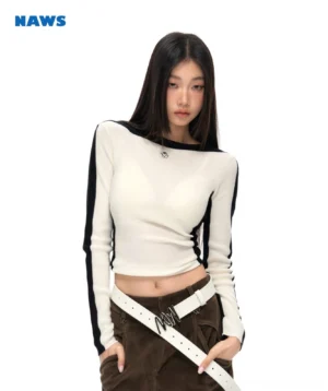 Female model wearing a striped shoulder fitted crop sweater with off-white knit body, navy blue contrast trim, and long sleeves in a minimalist studio