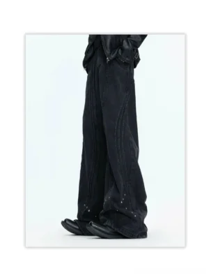 Side view of faded black wide-leg jeans showing curved panel seams, relaxed flowing fit, metallic studs, and alternative streetwear styling