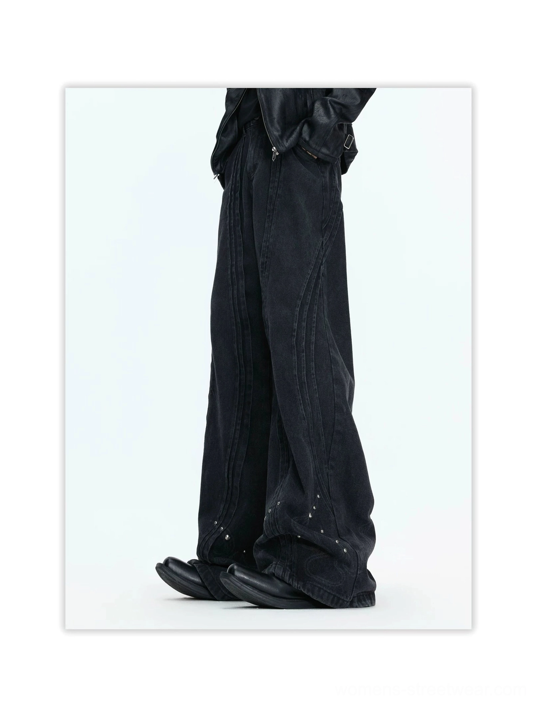Side view of faded black wide-leg jeans showing curved panel seams, relaxed flowing fit, metallic studs, and alternative streetwear styling