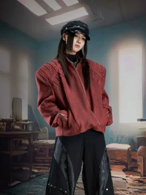 Burgundy red studded faux leather moto jacket with padded shoulders and stand collar shown on a female model in a vintage industrial studio