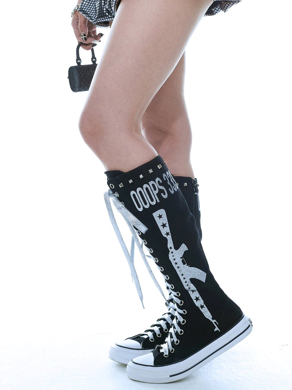 Side view of black studded graphic knee-high canvas boots with printed punk artwork, silver lacing, and white rubber outsole styled for Y2K streetwear