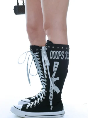 Model wearing black graphic canvas knee-high boots with silver laces and white rubber soles styled with a Y2K mini skirt and black handbag