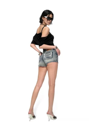 Full back view of fitted studded light wash denim cutoff shorts with embroidered back pockets, distressed finish, and frayed hems