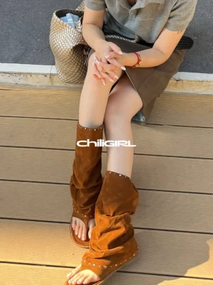 Model wearing brown studded suede thong sandal boots with a relaxed ruched shaft and open toe on outdoor wooden steps